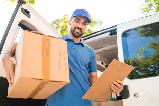Portrait of a delivery man unloading cardboard boxes from van and checking clipboard list. Delivery service and shipping concept.