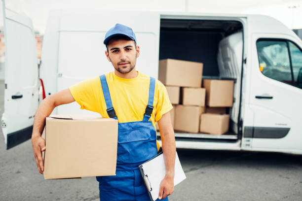 Cargo delivery service, male courier in uniform with box in hand and truck with cardboard parcels. Empty container